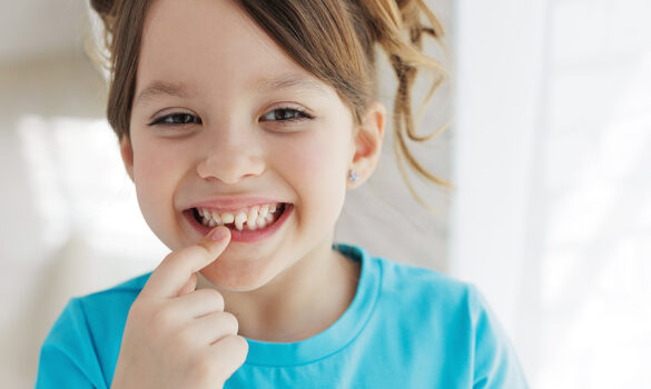 Picture of a young girl smiling, pointing at her mouth, and showing where she recently lost a tooth.